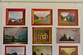 Landschaftsbilder Weiße Wand mit Hängebefestigung, darunter zwölf gerahmten Landschafts- und Naturgemälde, darunter eine Glasvase mit Blumen auf Tisch und ein Holzstock.