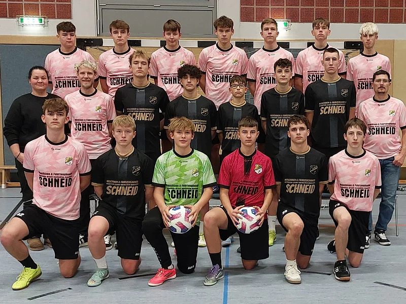 Mannschaftsfoto einer Fußballjugend in Sportkleidung in einer Sporthalle, 21 Personen in drei Reihen, zwei Spieler in der Mitte halten Bälle.