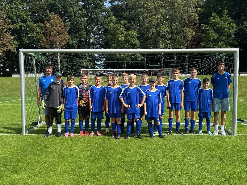 Jugendfußballmannschaft mit Trainern steht vor dem Tor auf dem grünem Spielfeld im Freien bei Tageslicht.