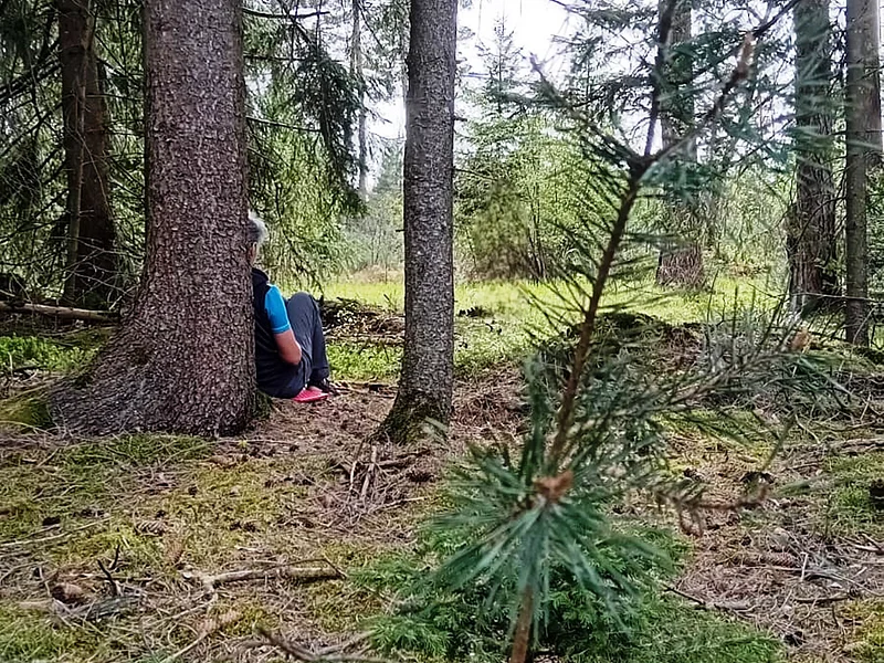 Waldbaden im Monheimer Wald Person sitzt im Wald auf dem Boden, lehnt an einem Baum. Umgebung aus Bäumen und Moos.