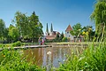 Sulzpark Beilngries Park mit Teich, Wiese, Bäumen und Menschen vor historischen Gebäuden mit zwei Türmen bei blauem Himmel