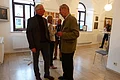 Ehrengäste bei der Eröffnung der Kunstausstellung Vier Personen unterhalten sich in einem hellen Raum mit Kunstwerken an den weißen Wänden und großen Fenstern mit Rundbögen oben. Im Raum sind Stehtische, Stühle und heller Bodenbelag.