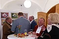 Ehrengäste bei der Eröffnung der Kunstausstellung Fünf Personen stehen um einen Stehtisch mit Getränken und Herbstdekoration in einem hellen Raum mit Gemälden an der Wand.